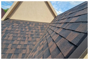 Detailný záber na šikmú strechu s Asfaltovým strešným šindeľom Katepal Mansion - hneďý od spoločnosti KATEPAL Oy, ktorý sa vyznačuje čistými líniami a sýtymi hnedými tónmi pod čiastočne zamračenou modrou oblohou.