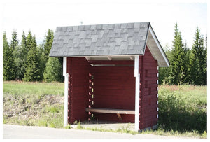 Malý červený drevený autobusový prístrešok so sivou strechou z Asfaltový strešný šindeľ Katepal Rocky - grafitová šedá od KATEPAL Oy stojí pri ceste, obklopený zelenou trávou a stromami pod jasnou oblohou.