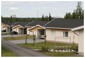 Rad moderných jednoposchodových domov s KATEPAL Oy Asfaltový strešný šindeľ Katepal Rocky - grafitová šedá na sivých strechách, svetlých stenách a príjazdových cestách stojí v prímestskej štvrti ohraničenej zelenými trávnikmi a stromami.