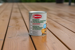 Na hladkej, čerstvo dokončenej drevenej terase v exteriéri leží plechovka s ochranným náterom na drevo Owatrol Aquatherm. Na plechovke je text v českom a slovenskom jazyku a modrý symbol environmentálnej značky.